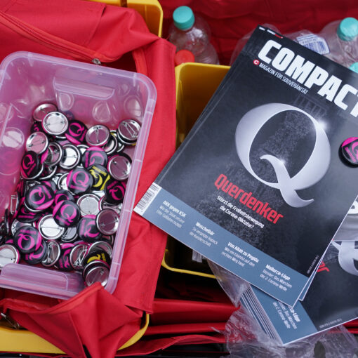 BERLIN, GERMANY - AUGUST 28: Querdenker Q buttons lie in a bin for sale next to copies of the right-wing magazine Compact at a gathering of coronavirus skeptics on the eve of a planned protest march on August 28, 2020 in Berlin, Germany. Tens of thousands of protesters from a wide range of backgrounds, from people who doubt the danger of the coronavirus pandemic to conspiracy theorists to right-wing extremists, are expected to participate in tomorrow's protests and march. The march is being organized by Querdenker 711, a Stuttgart-based group that sees the pandemic as a conspiracy. Many Querdenker followers also sympathize with the QAnon movement. (Photo by Sean Gallup/Getty Images)